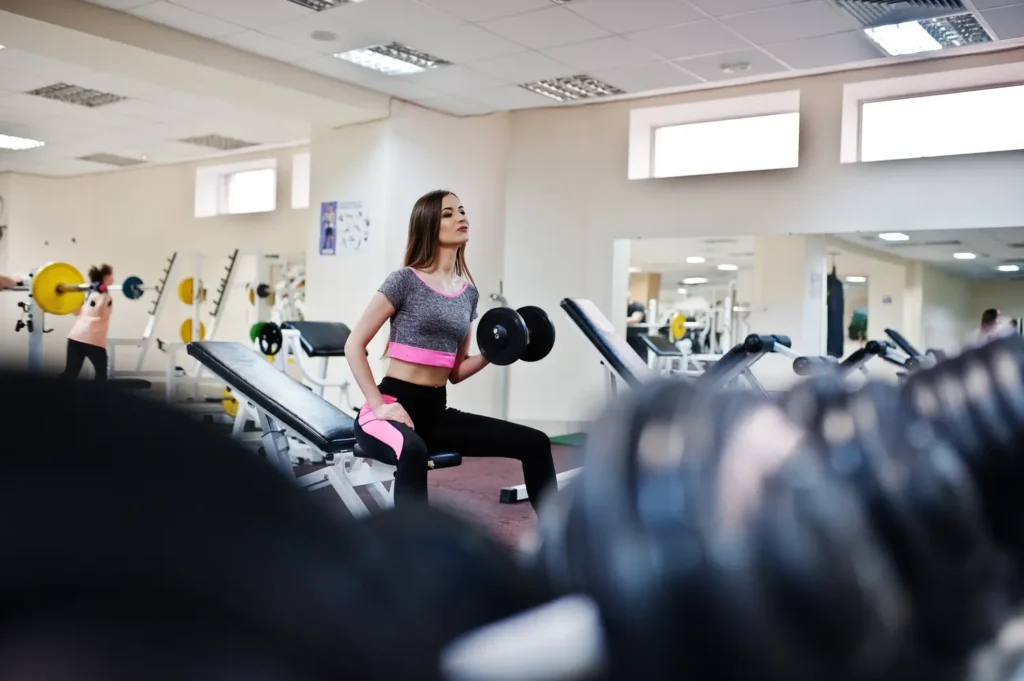 Mujer joven entrenando en el gimnasio con pesas hábitos saludables para aumentar masa muscular-clinica de fitness